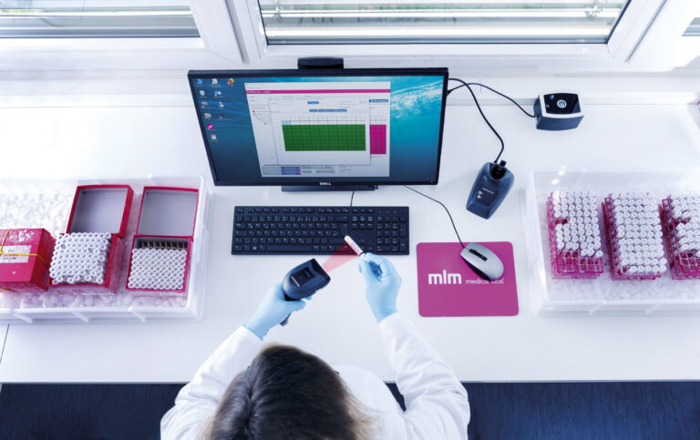 Laboratory technician using a barcode scanner to manage samples, with a computer displaying data, illustrating the efficiency of MLM Medical Labs' biological sample storage service